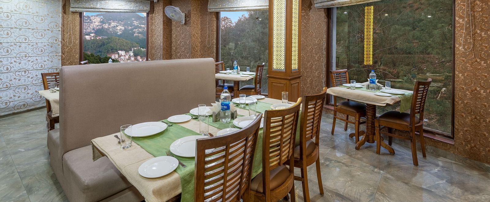 Dining area with a table set for a meal, featuring plates and water bottles, with a mountain view visible through the window at DLS Hotels The Rock Castle.